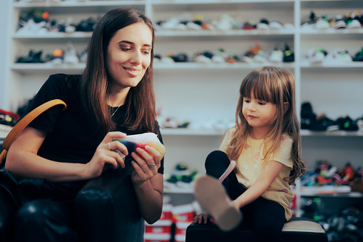 Mom helping her little girl finding well sitting footwear