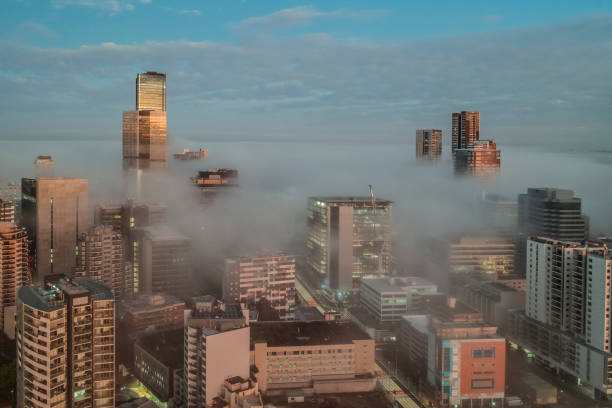 Morning sunrise aerial photo of fog and mist engulfing and enveloping office towers in a downtown city district. Fog moving at low levels amongst tall buildings.