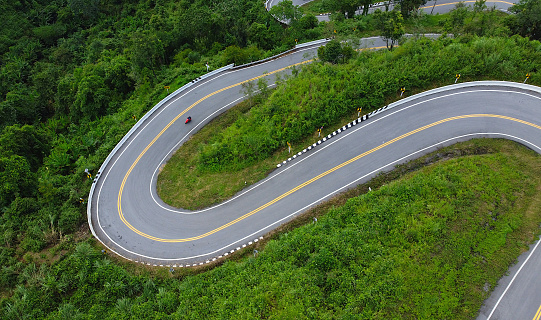 Aerial view of a winding road with motorcycles riding through a dense forest.