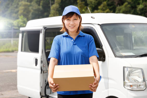Woman in blue polo shirt and hat carrying cardboard boxes. She works as a mover and courier. stock photo