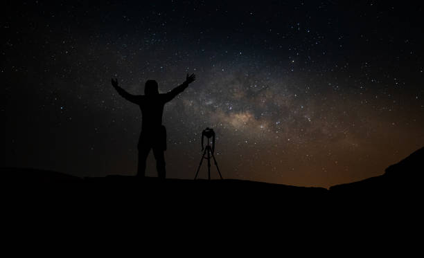 milky way. night sky with stars and silhouette of a standing mountaineer man with yellow light on the mountain. space background - milky way galaxy space star imagens e fotografias de stock