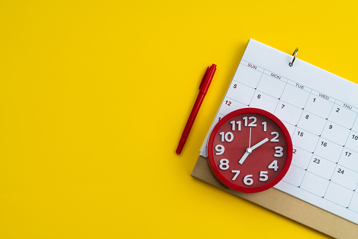 Calendar and alarm clock on yellow background.