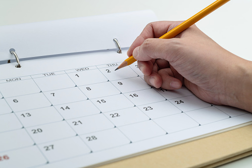 Woman hand with pencil writing on calendar page