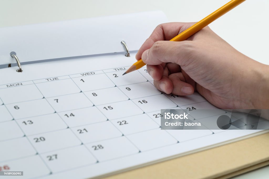 Woman hand with pencil writing on calendar page Woman hand with pencil writing on calendar page. Calendar Stock Photo