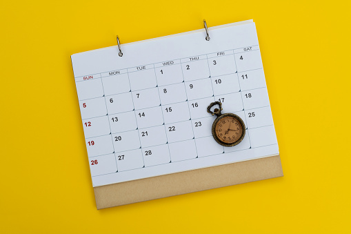 Calendar and pocket watch on yellow background.