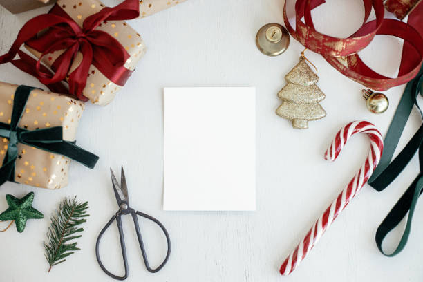 istock Christmas card mockup. Empty greeting card flat lay with christmas gift, decorations, ribbons, ornaments on white rustic table. Postcard template with space for text. Happy Holidays! 1418944767