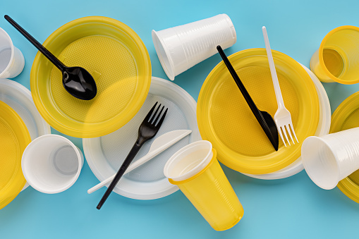 A set of disposable, yellow and white, plastic utensils. Gray background, copy space. The concept of ecology and recycling of plastic waste.