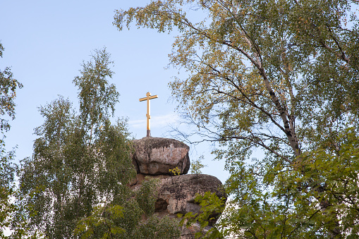 Metallic catholic cross on rock pedestal, with a blue sky with clouds in the background. Copy space.