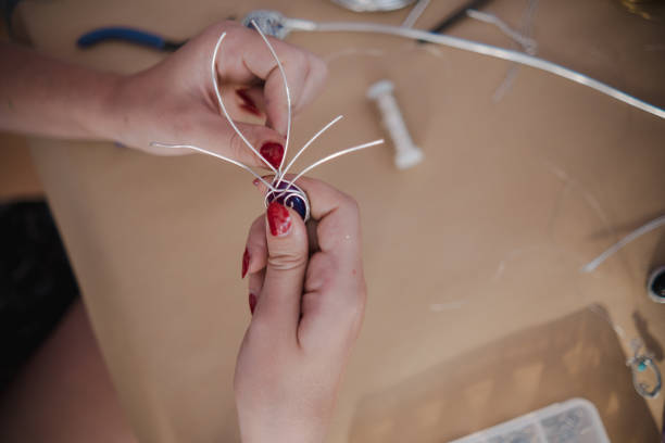 Woman using different tools and a silver wire to create a unique pendant with a crystal in centerpiece