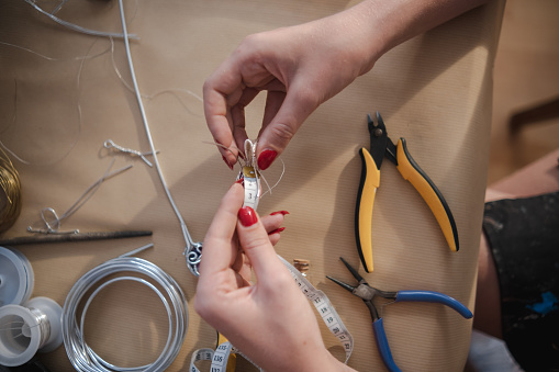 Woman using different tools and a silver wire to create a unique pendant with a crystal in centerpiece