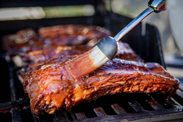 costillas de ternera siendo bañadas con salsa barbacoa en una parrilla con un cepillo de bastidor - costilla fotografías e imágenes de stock