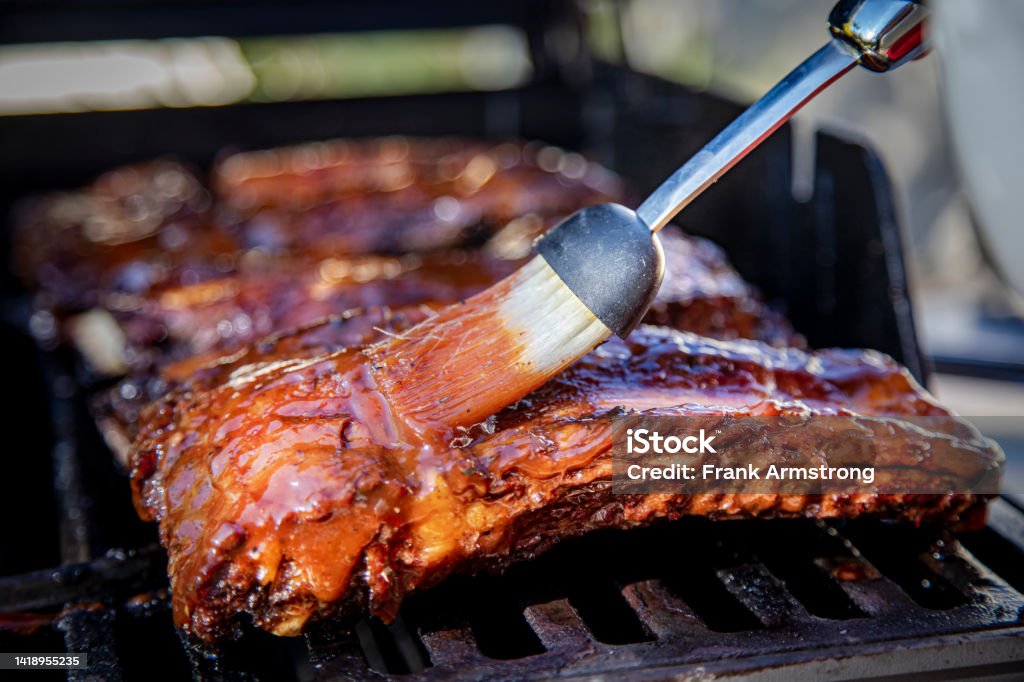 Beef ribs being basted with bbq sauce on a grill with a basting brush Barbecue Grill Stock Photo