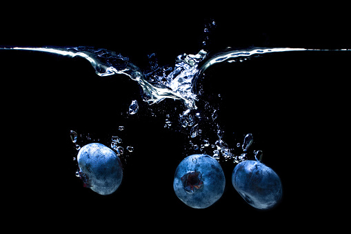 Blueberries sinking underwater with air bubbles and splashes isolated on black background.