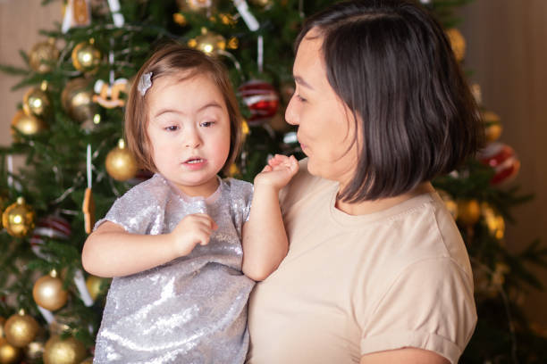 cute baby with down syndrome with mom near the christmas tree, happy new year and Christmas stock photo