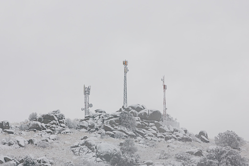 Three cell towers on a mountain peak in a snowfall.