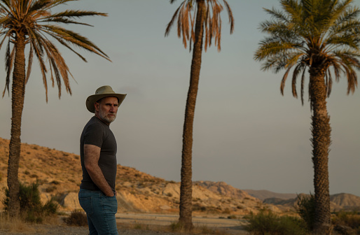 Adult man in cowboy hat in desert with palm trees. Almeria, Spain