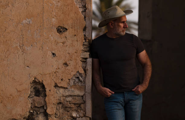 ritratto di uomo adulto in cappello da cowboy e jeans contro l'edificio abbandonato durante il tramonto - the western wall foto e immagini stock