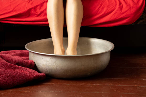 a girl washes her feet in an aluminum basin with water on a wooden floor at home, foot care, wash feet at home, hygiene a girl washes her feet in an aluminum basin with water on a wooden floor at home, foot care, wash feet at home, hygiene, swim in a basin home pedicure stock pictures, royalty-free photos & images