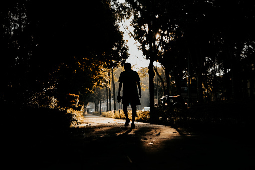 silhouette rear view mid adult man walking in park footpath with backlit sunlight after routine running exercise