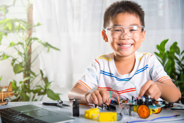 istock Asian kid boy plugging energy and signal cable to sensor chip with open-source hardware and software robot car 1418976243