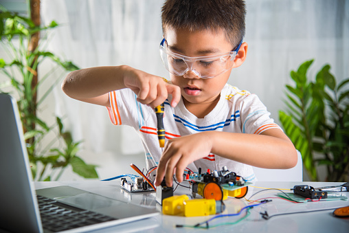 Asian kid boy assembling the open-source hardware and software robot car homework project at home