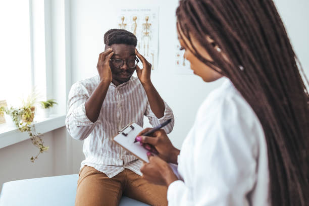 mężczyzna dotyka skroni, wyjaśniając swój ból głowy troskliwej lekarce. - doctor patient doctors office teenager zdjęcia i obrazy z banku zdjęć