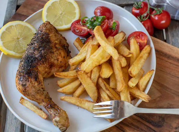 Homemade fresh cooked crispy chicken leg. Served with homemade french fries and tomato salad on a plate on wooden background