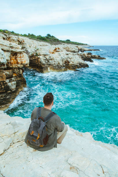 istock man with backpack sitting on the cliff enjoying city view 1418980529