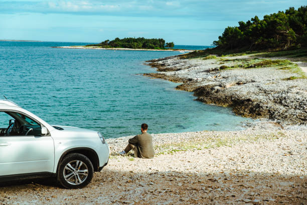 istock man standing near car at seaside. road trip concept 1418980562