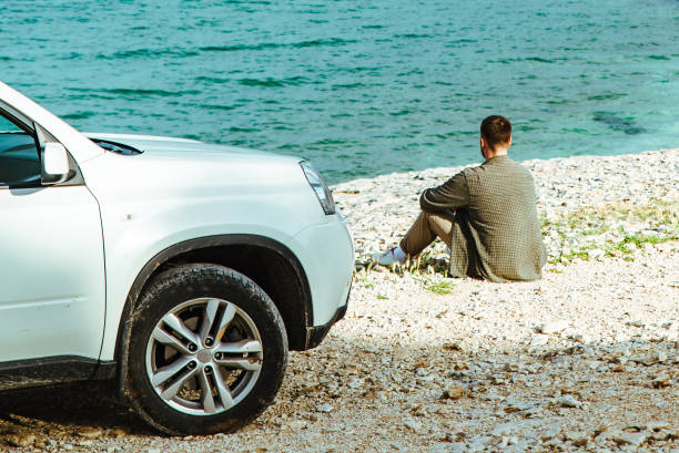 istock man standing near car at seaside. road trip concept 1418980565