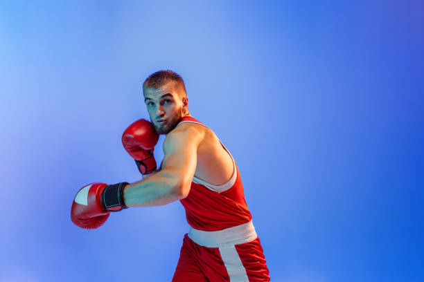 istock Knockout punch. Male boxer in red uniform and boxing gloves training isolated on blue background in neon. Strength, attack and motion concept. 1418988593