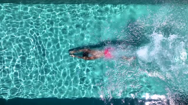 Aerial top view of a man diving into fresh swimming pool water