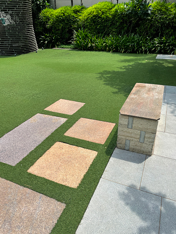 Stock photo showing close-up, elevated view of paved patio area of garden besides a fake grass lawn with rectangular, paved stepping stones.