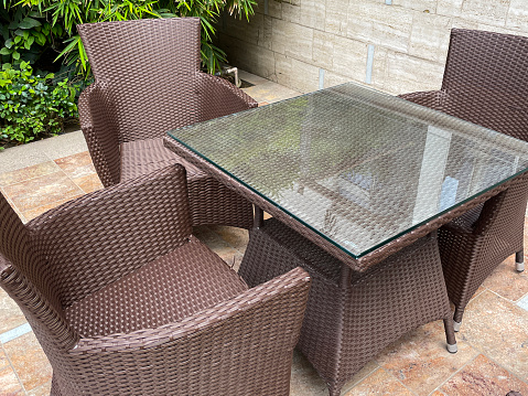 Stock photo showing rattan and glass topped patio table surrounded by rattan wickerwork chairs pictured outside on a paved travertine stone patio.