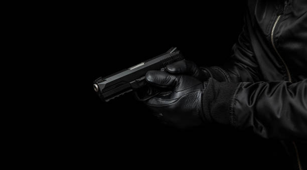 istock A man in a black jacket and black gloves holding a gun. Dark background. 1419001272