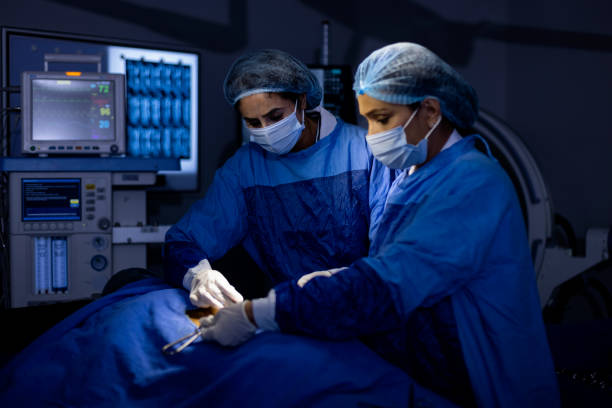 Female surgeons operating patient at hospital Two female surgeons performing surgery at hospital operating room surgical needle stock pictures, royalty-free photos & images