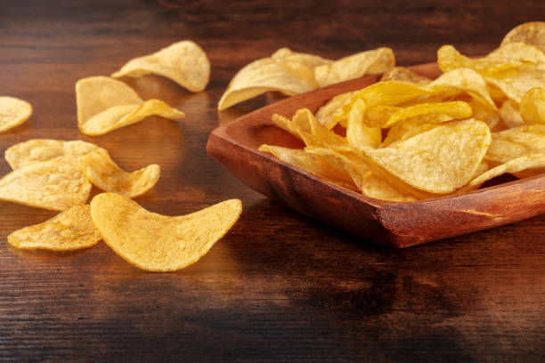 istock Potato chips or crisps in a bowl and scattered on a wooden table 1419006892