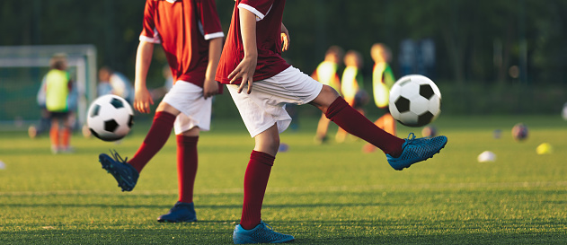 Two football players juggle soccer balls. Kids practicing soccer on grass pitch