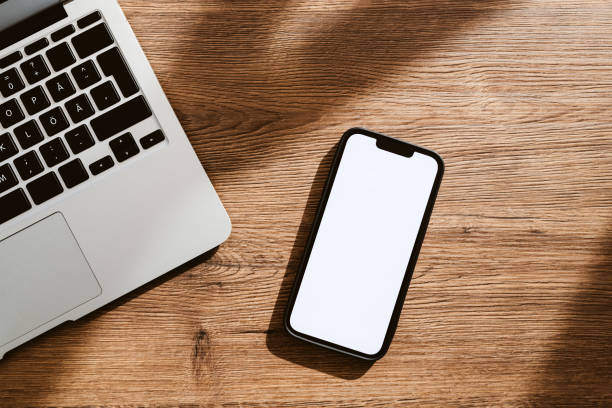 istock Mobile phone with blank white mockup touchscreen and laptop computer on office desk, top view 1419009302