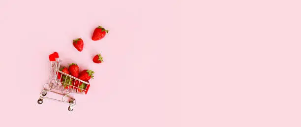 Fresh red strawberry in shopping cart on pink background. Online shopping and Valentines Day minimalistic concept. Black Fridays sales banner. Healthy, organic, vegan food