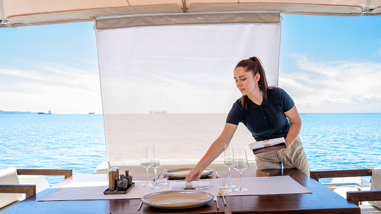 Stewardess arranging cutlery on table on luxury yacht.