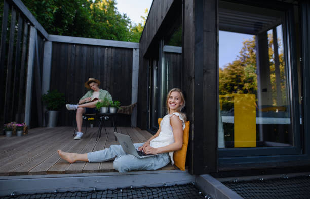 Happy young couple with laptop resting outdoors in a tiny house, weekend away and remote office concept. A happy young couple with laptop resting outdoors in a tiny house, weekend away and remote office concept. tiny house stock pictures, royalty-free photos & images