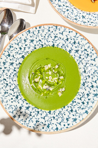 Composition with vegetable soup in ceramic bowl. Green soup with broccoli and cheese on summer day. Italian soup with green pea. Vegan menu. Hot dishes. Vegetables food. Eat less meat