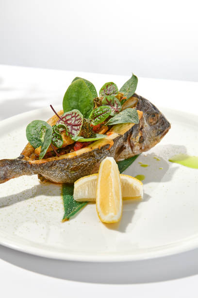 istock Whole roasted fish with spinach leaves on white plate. Grilled dorado on light background in summer menu. Healthy food - Roasted dorado fish. Concept menu with hard shadows. 1419017822