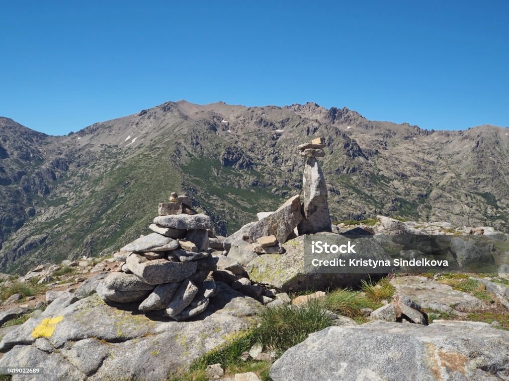 scenery of high mountainn peaks in corsician alpes with green bushes and rocks pile cairns marked path on gr20 trek and white clouds blue sky Beauty Stock Photo
