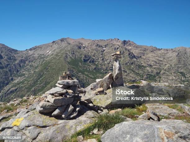 Scenery Of High Mountainn Peaks In Corsician Alpes With Green Bushes And Rocks Pile Cairns Marked Path On Gr20 Trek And White Clouds Blue Sky Stock Photo - Download Image Now