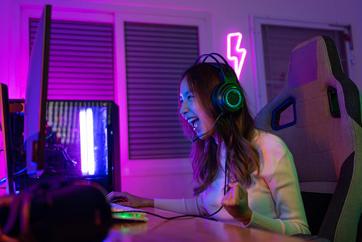 Asian gamer playing online video game winning excited on PC with lighting effect, broadcast streaming live at home. Gamer and E-Sport online gaming technology Championship tournament gamer concept.