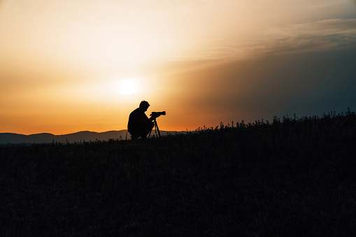 Silhouette of a photographer at sunset. He's holding his camera. Copy space.