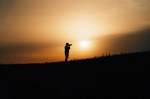 Silhouette of a photographer at sunset. He's holding his camera. Copy space.