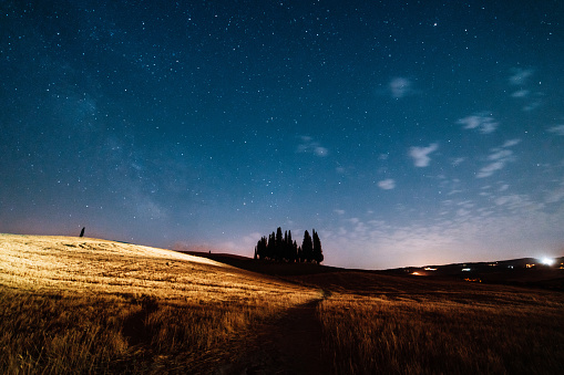 Starry sky over San Quirico d'Orcia cypresses at night. Famous location in Tuscany, Italy.
